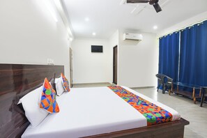 Habitación de hotel con cama, escritorio, silla, ventana con cortinas y unidad de aire acondicionado.