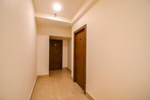 A hallway with a wooden door on the right and a closed door at the end. - FabHotel Moubani Residency (Barasat)