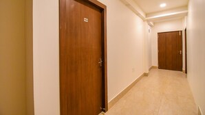 A hallway with wooden doors, a tiled floor, and a ceiling with recessed lighting. - FabHotel Moubani Residency (Barasat)