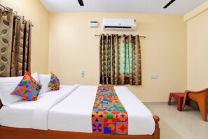 Een hotelkamer met een bed, gordijnen, een airconditioner en een kleine tafel.