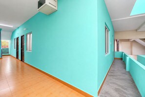 Un couloir aux murs de couleur turquoise, doté d’un plancher en bois et d’un appareil de climatisation fixé au plafond.