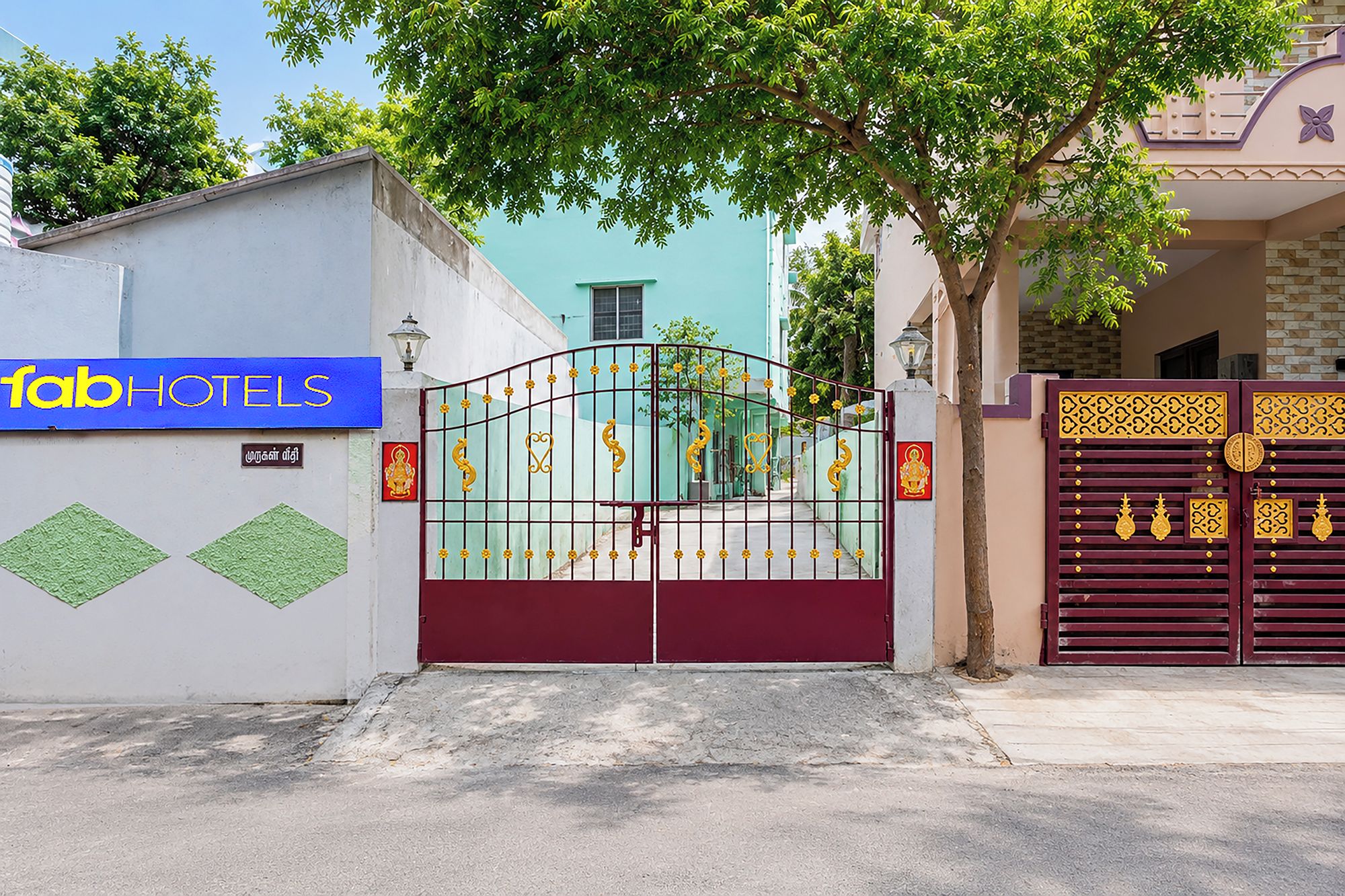 L’entrée d’un hôtel, avec une allée bordée de grilles, un panneau indiquant « hôtels de luxe », et un portail décoratif orné de motifs dorés.
