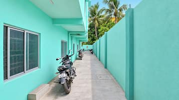 Un pasillo con paredes azul turquesa, flanqueado por motocicletas estacionadas, y un cielo despejado.