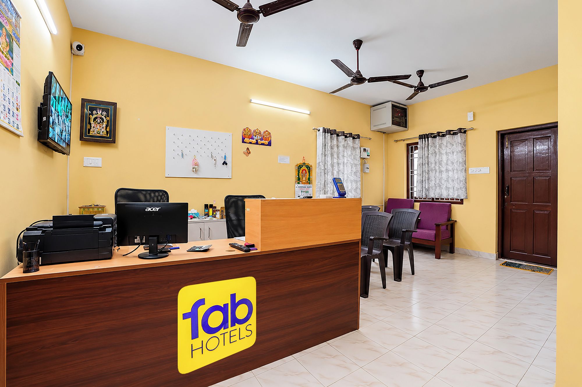 A hotel reception area with a wooden desk, computers, and a seating area with chairs and a sofa.