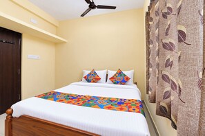 Una habitación de hotel con cama, ventilador de techo, cortina estampada y puerta de madera.
