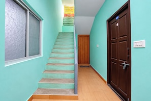 Un escalier menant à une porte avec une plaque numérotée, une fenêtre avec du verre dépoli et un mur peint en bleu clair.