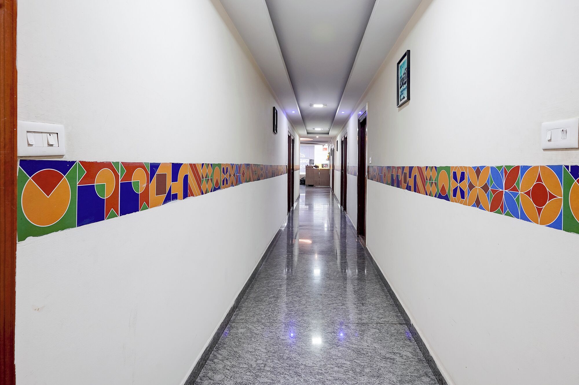 A hotel corridor with a tiled wall design, a polished floor, and a ceiling with recessed lighting.