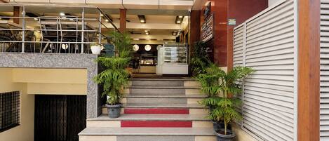 A hotel lobby with a staircase leading to a second floor, a reception desk, and a closed shutter on the right.