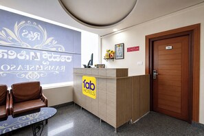 Zona de recepción de un hotel con mostrador, un área de descanso con sillas, una puerta de madera y una pared con texto decorativo.