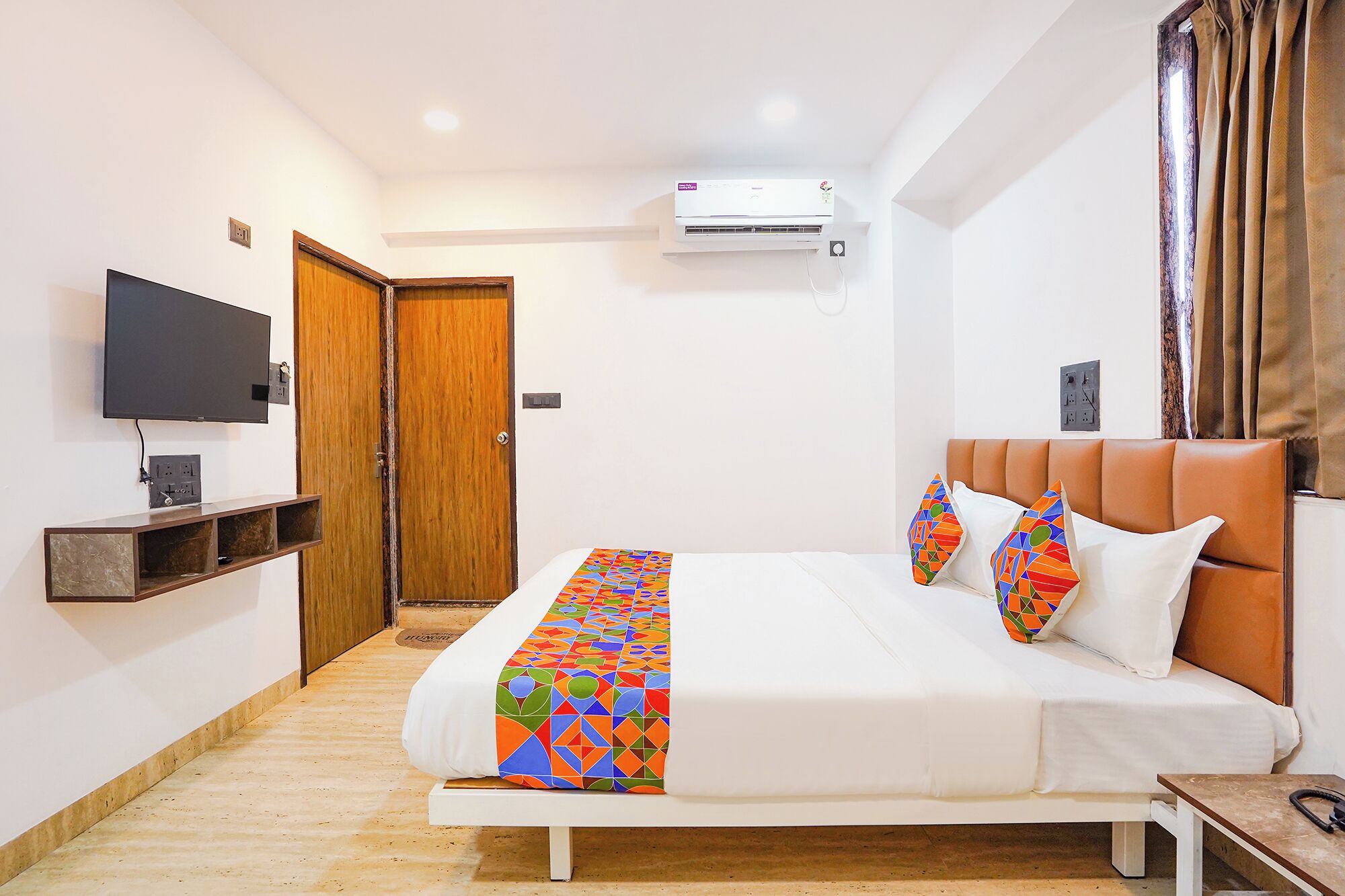 Una habitación de hotel con cama, televisor, aire acondicionado y una puerta de madera.