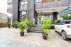 Fachada de hotel de diseño moderno, con una escalera que conduce a la entrada, plantas en macetas y un coche estacionado.