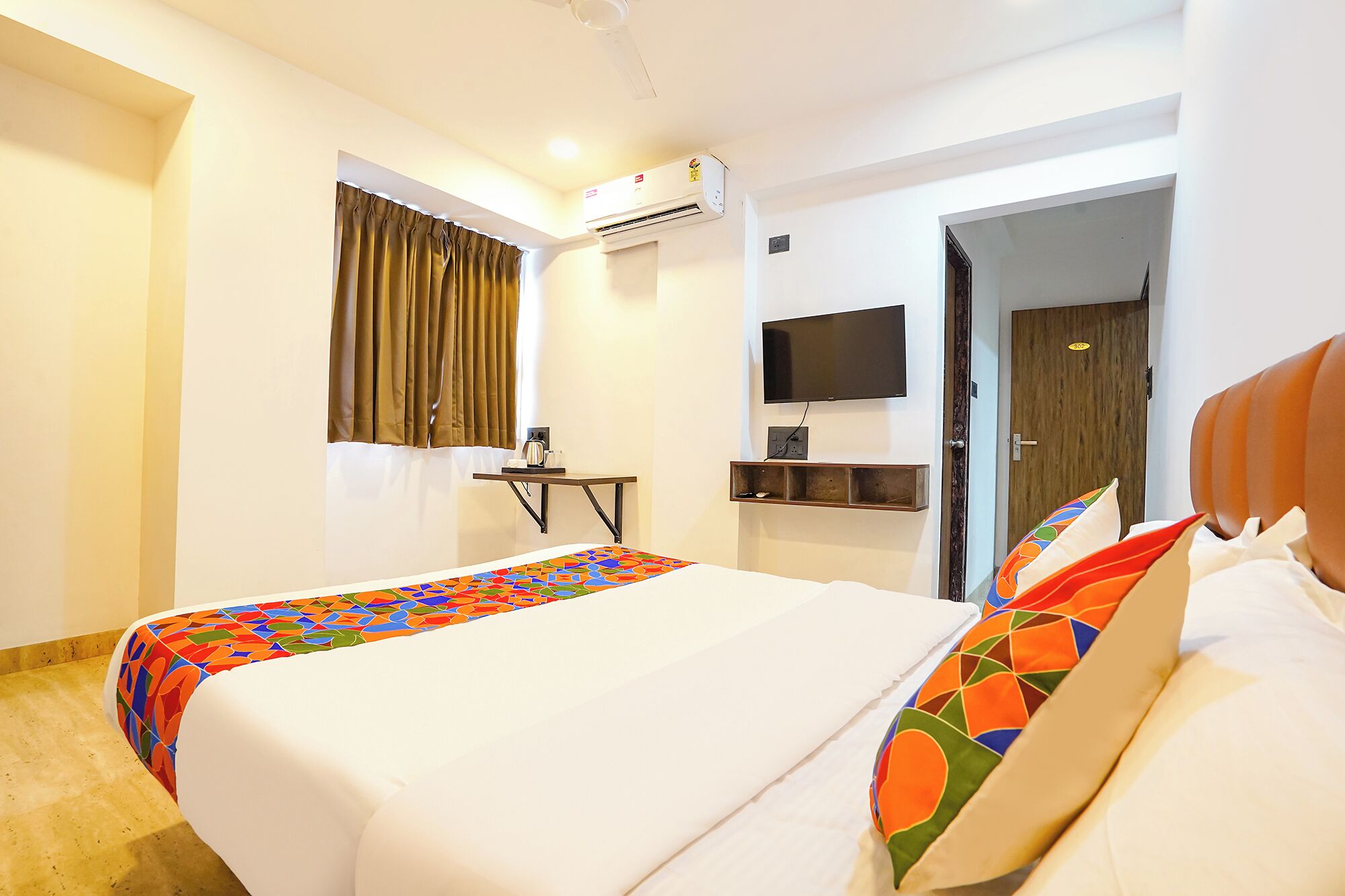Quarto de hotel com uma cama, uma televisão na parede, um aparelho de ar condicionado e uma porta com um número.