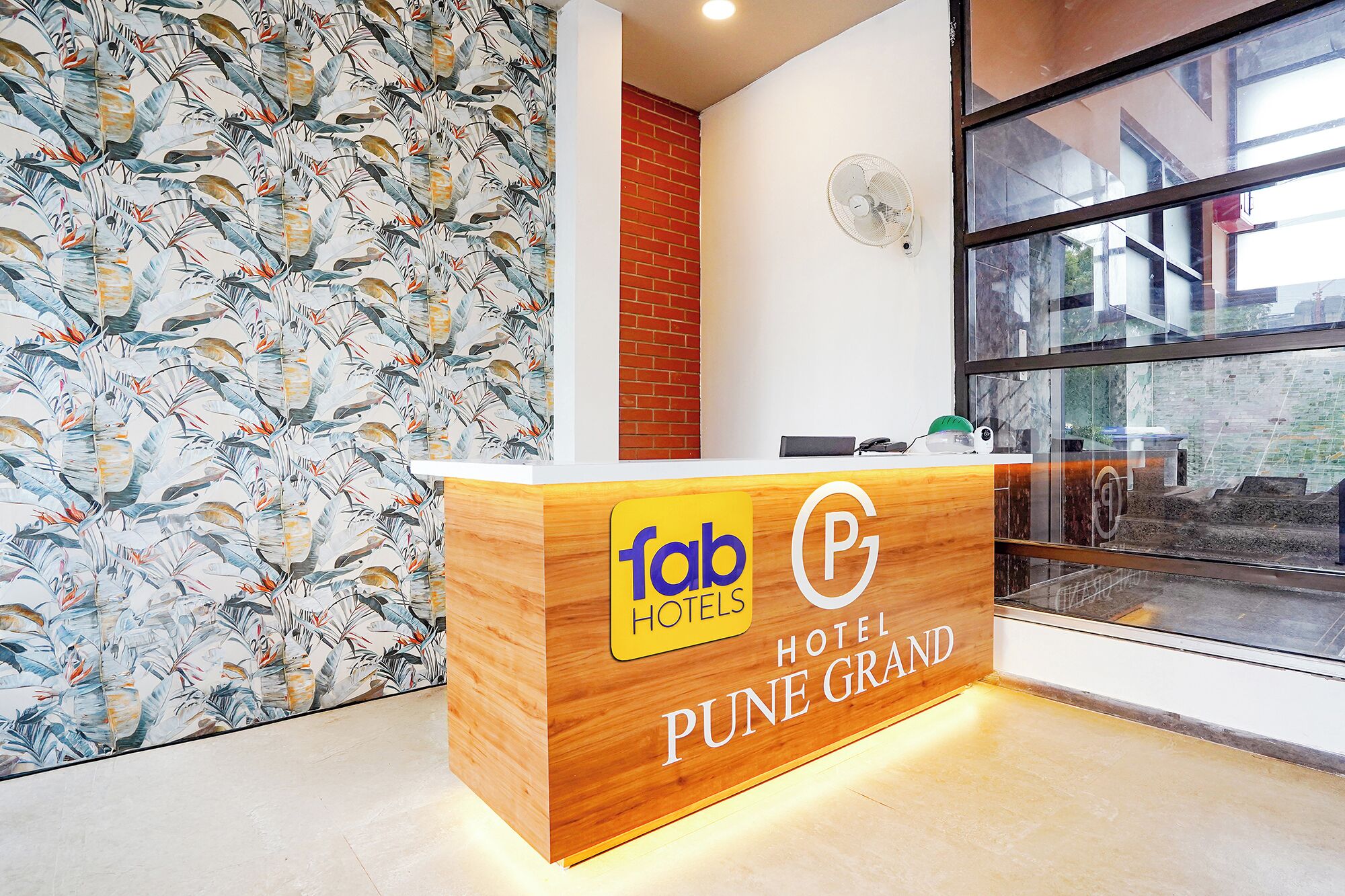 A reception desk with a wooden finish, a logo for 'fab hotels,' and the name 'PUNE GRAND' indicating the hotel.
