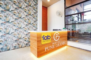Uma receção com acabamento em madeira, o logótipo 'fab hotels' e o nome 'PUNE GRAND' a indicar o hotel.