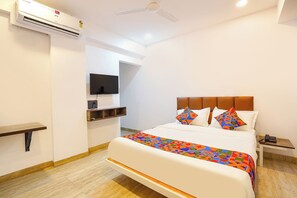 Quarto de hotel com uma cama, televisão presa à parede, mesa de cabeceira e tomada.