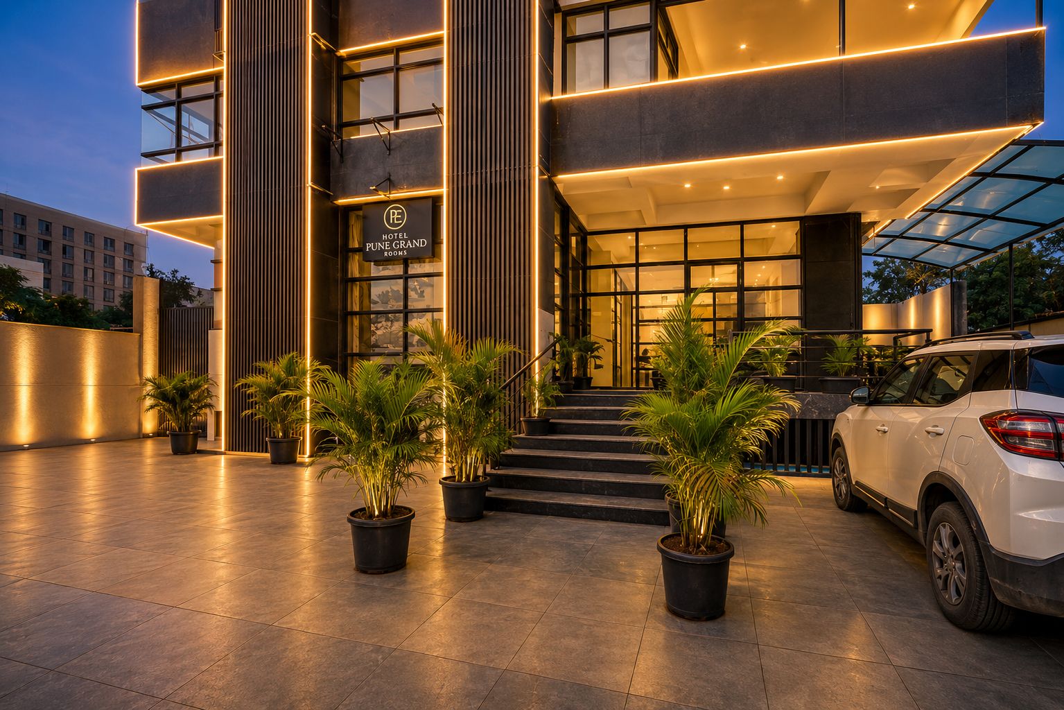 A hotel entrance with a modern design, featuring a sign for 'Hotel Pune Grand Rooms' and a car parked in front.