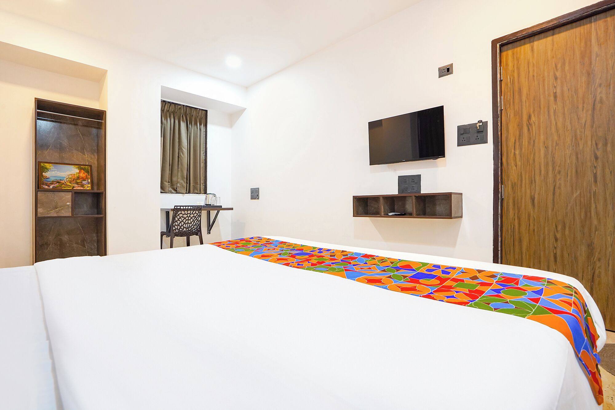 Ein Hotelzimmer mit Bett, Schreibtisch, Stuhl, Fernseher und Kleiderschrank.
