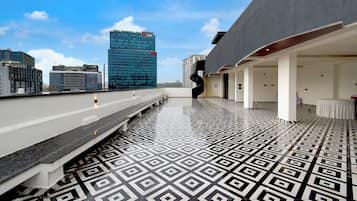 A rooftop terrace with a geometric patterned floor, a modern building with a glass facade, and a clear sky.