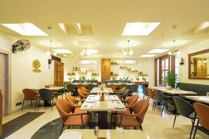 A restaurant with multiple dining tables and chairs, ceiling fans, and decorative wall shelves.
