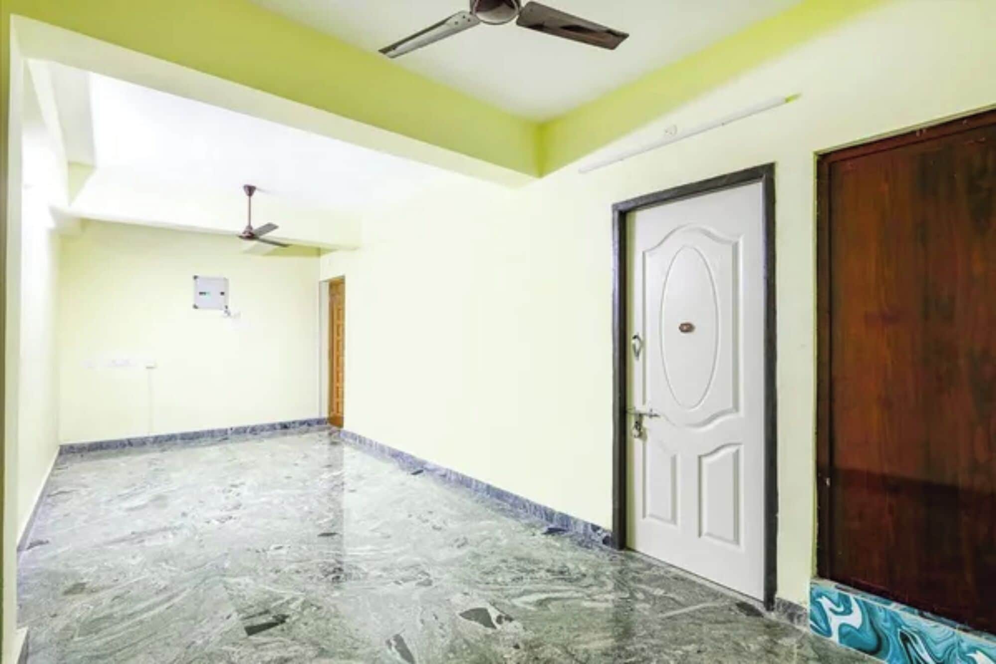 Un pasillo con suelo de mármol, ventilador de techo, una puerta blanca y una puerta de madera.