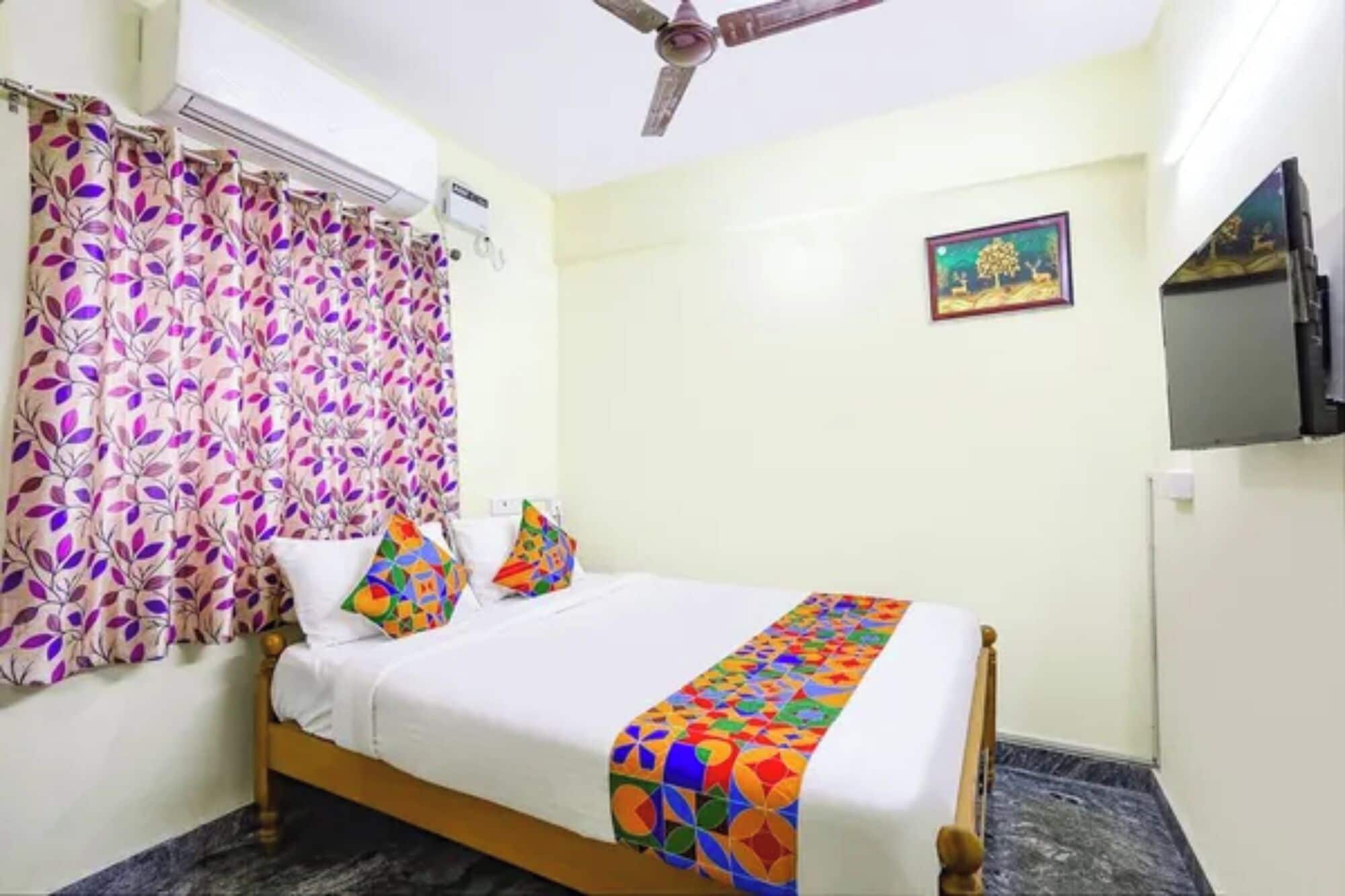 A bedroom with a bed, a ceiling fan, a TV, and a painting on the wall.