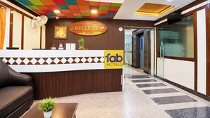 Zona de recepción de un hotel con un mostrador, un sofá, una planta pequeña y un cartel que indica la recepción.