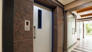 Un ascensor con pantalla digital, botón de llamada y puerta con marco azul.