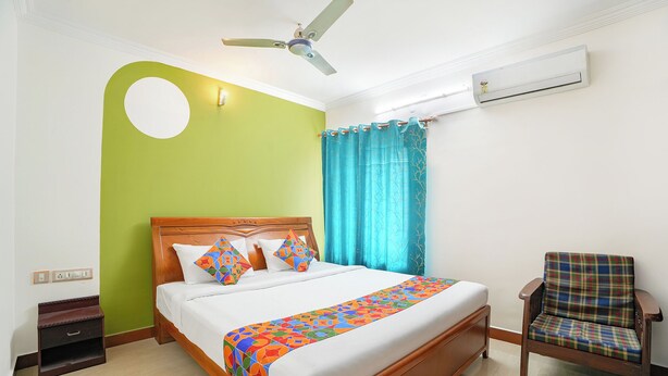 Una habitación de hotel con una cama, una silla, un ventilador de techo, un equipo de aire acondicionado y una ventana con cortinas.