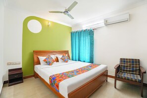 Une chambre d’hôtel équipée d’un lit, d’une chaise, d’un ventilateur de plafond, d’un climatiseur et d’une fenêtre avec des rideaux.