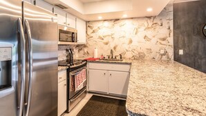 A modern kitchen with stainless steel appliances, a granite countertop, and a hexagonal tile backsplash. - Lakeside Oasis Fort Myers (Fort Myers)