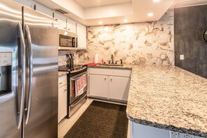 A modern kitchen with stainless steel appliances, a granite countertop, and a hexagonal tile backsplash. - Lakeside Oasis Fort Myers (Fort Myers)
