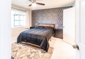 Une chambre à coucher avec un lit, un ventilateur de plafond, un mur à motifs, une porte et une fenêtre avec des rideaux.