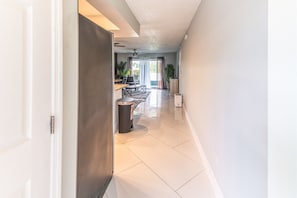 A hallway with a closed door, a trash bin, and a kitchen area with a dining table and chairs. - Oasis on the Shore of Lake Fort Myers (Fort Myers)