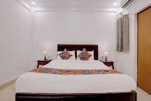 Habitación de hotel con cama, dos mesitas de noche con lámparas, cabecero de madera y puerta de madera.
