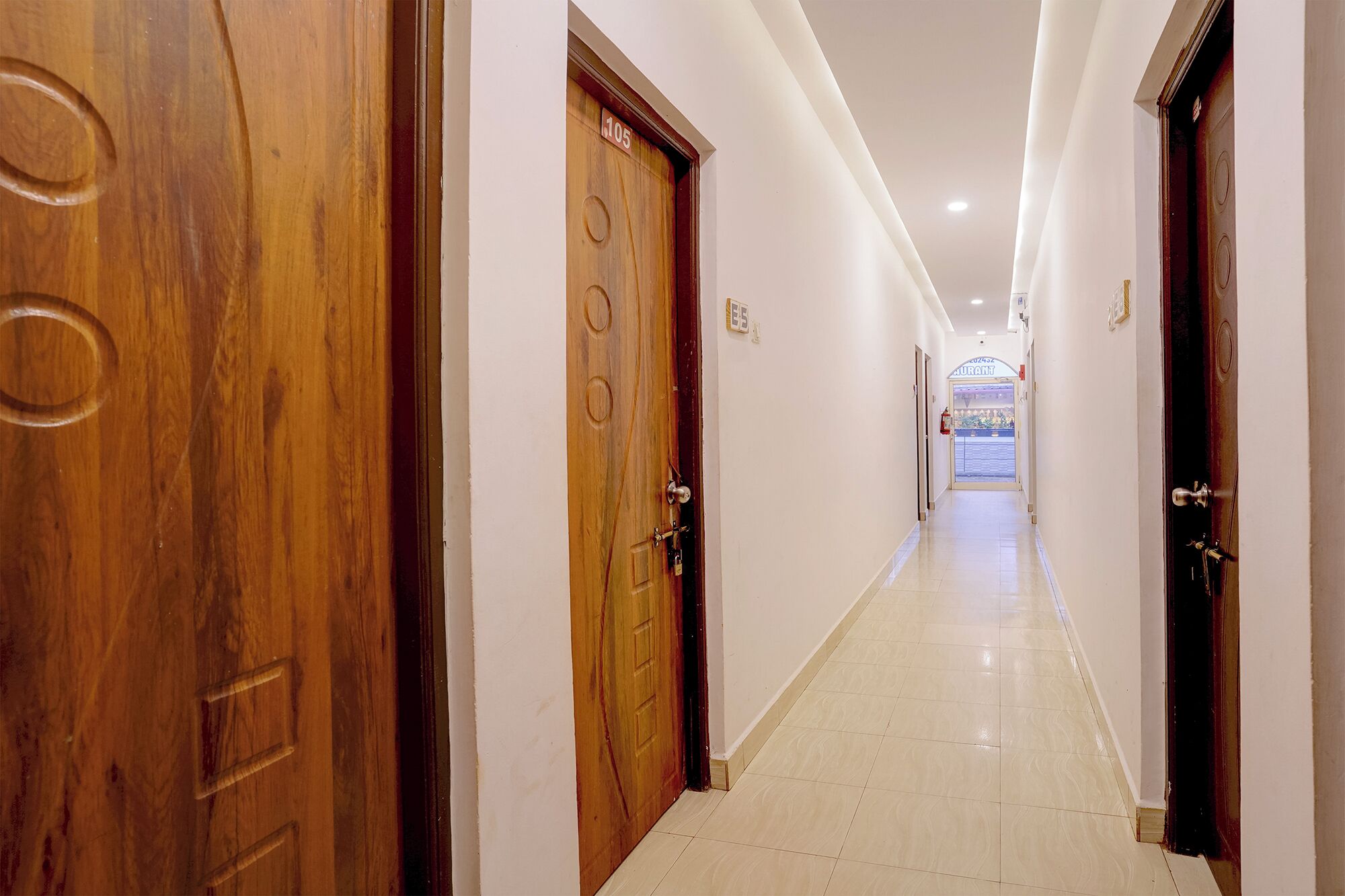 Pasillo de hotel con puertas de madera, piso de baldosas y un letrero que indica un restaurante.