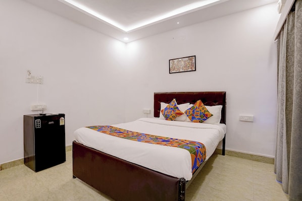 A hotel room with a bed, a small refrigerator, and a ceiling light fixture.