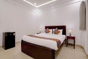 Una habitación de hotel con cama, mesitas de noche, un armario y un escritorio pequeño.