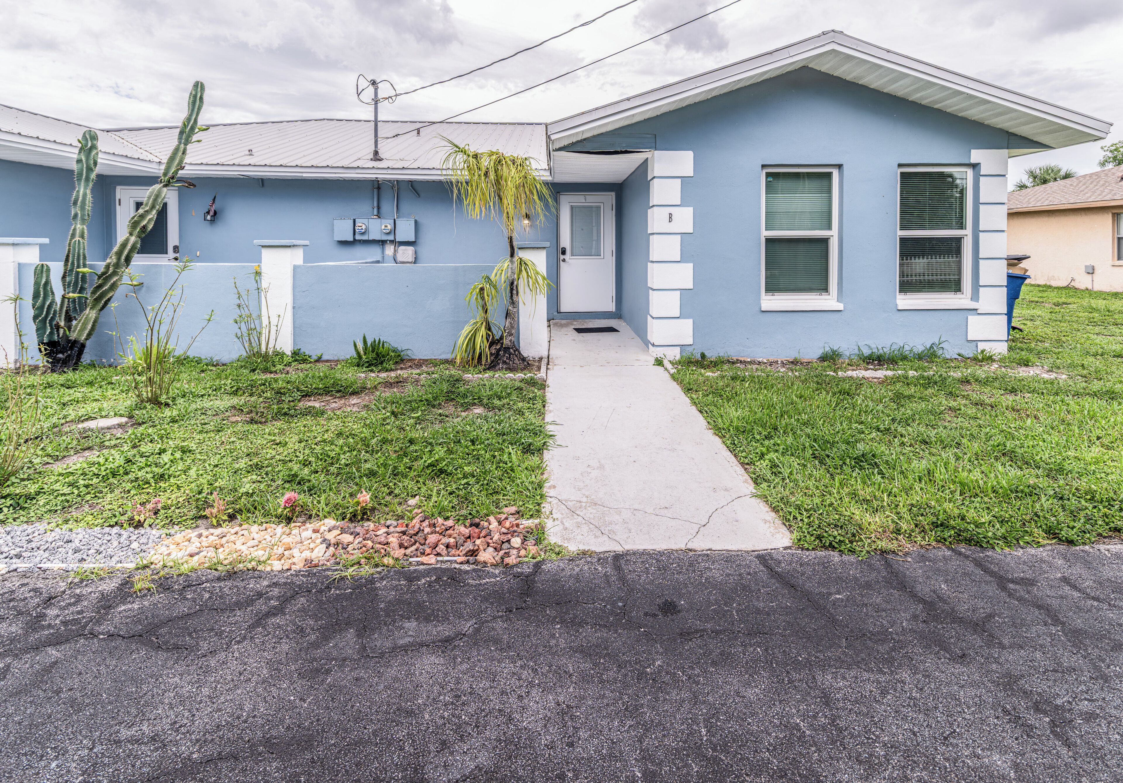 A residential house with a blue exterior, a concrete driveway, and a cactus in the front yard.