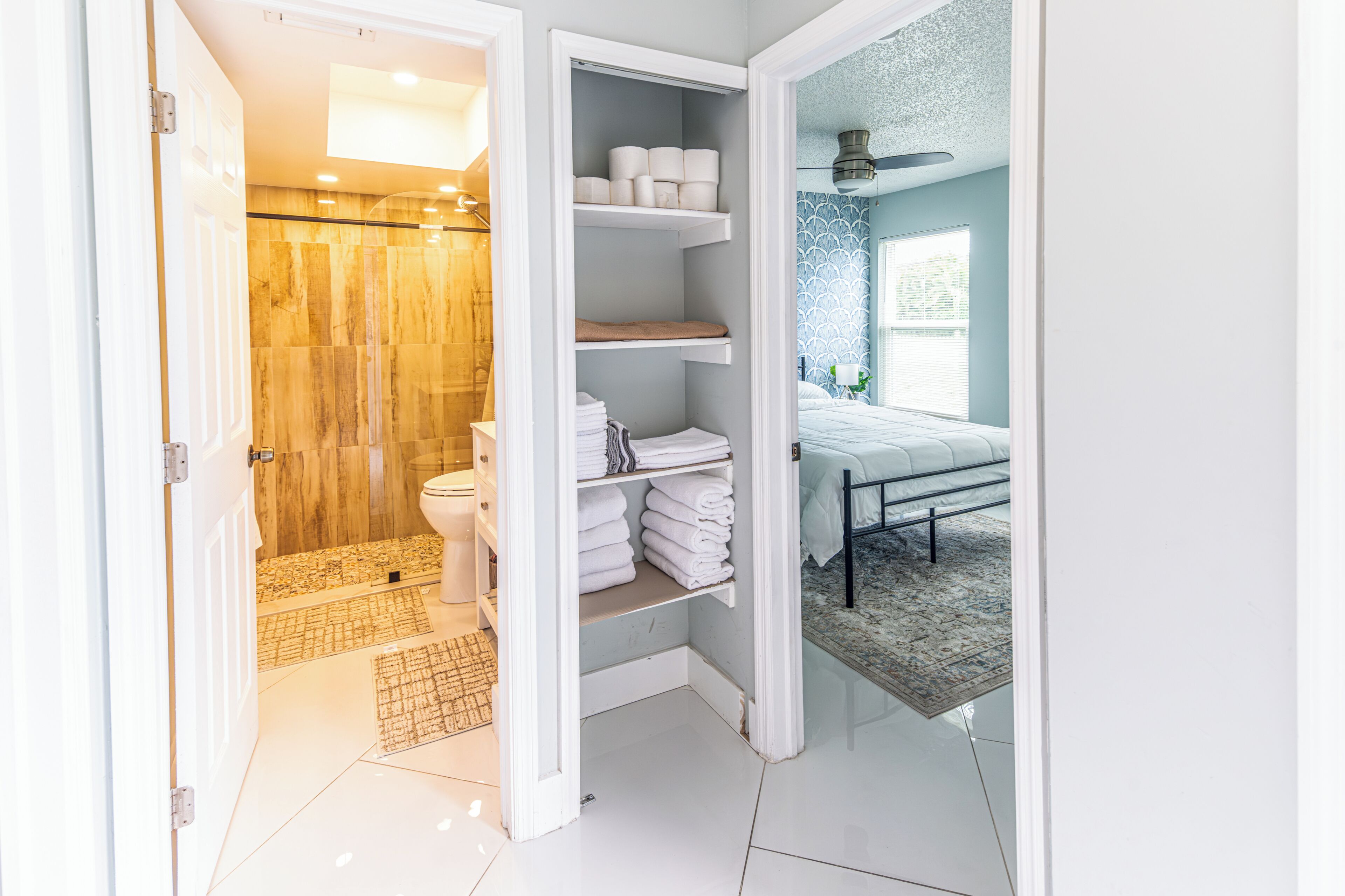 A bathroom with a shower, toilet, and shelves with towels.
