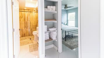 A bathroom with a shower, toilet, and shelves with towels.
