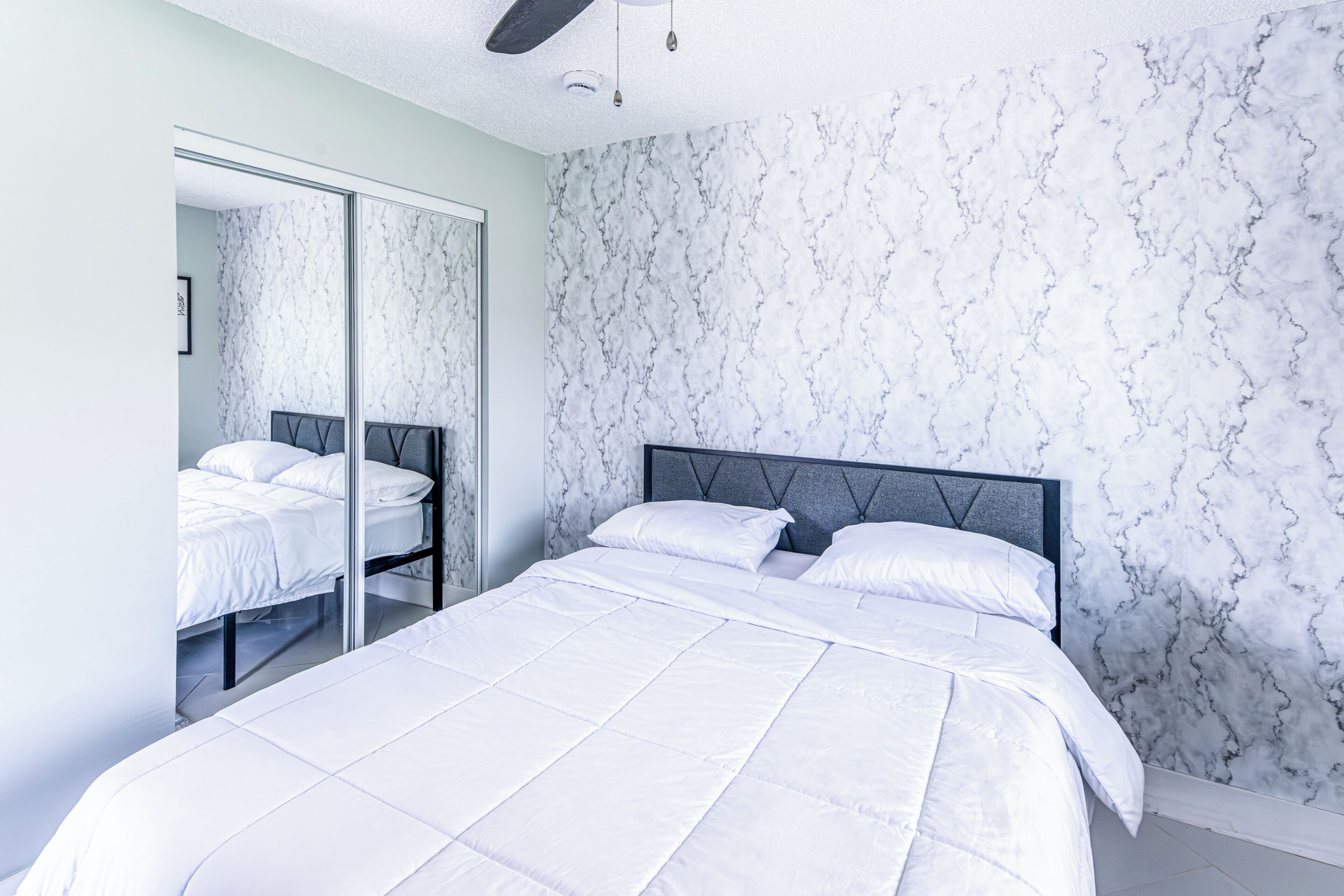 A bedroom with a bed, a wardrobe, and a marble-patterned wall.