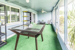 A room with a glass-top table, green artificial turf, a ceiling fan, and large windows with blinds. - Lakeside Oasis Fort Myers (Fort Myers)