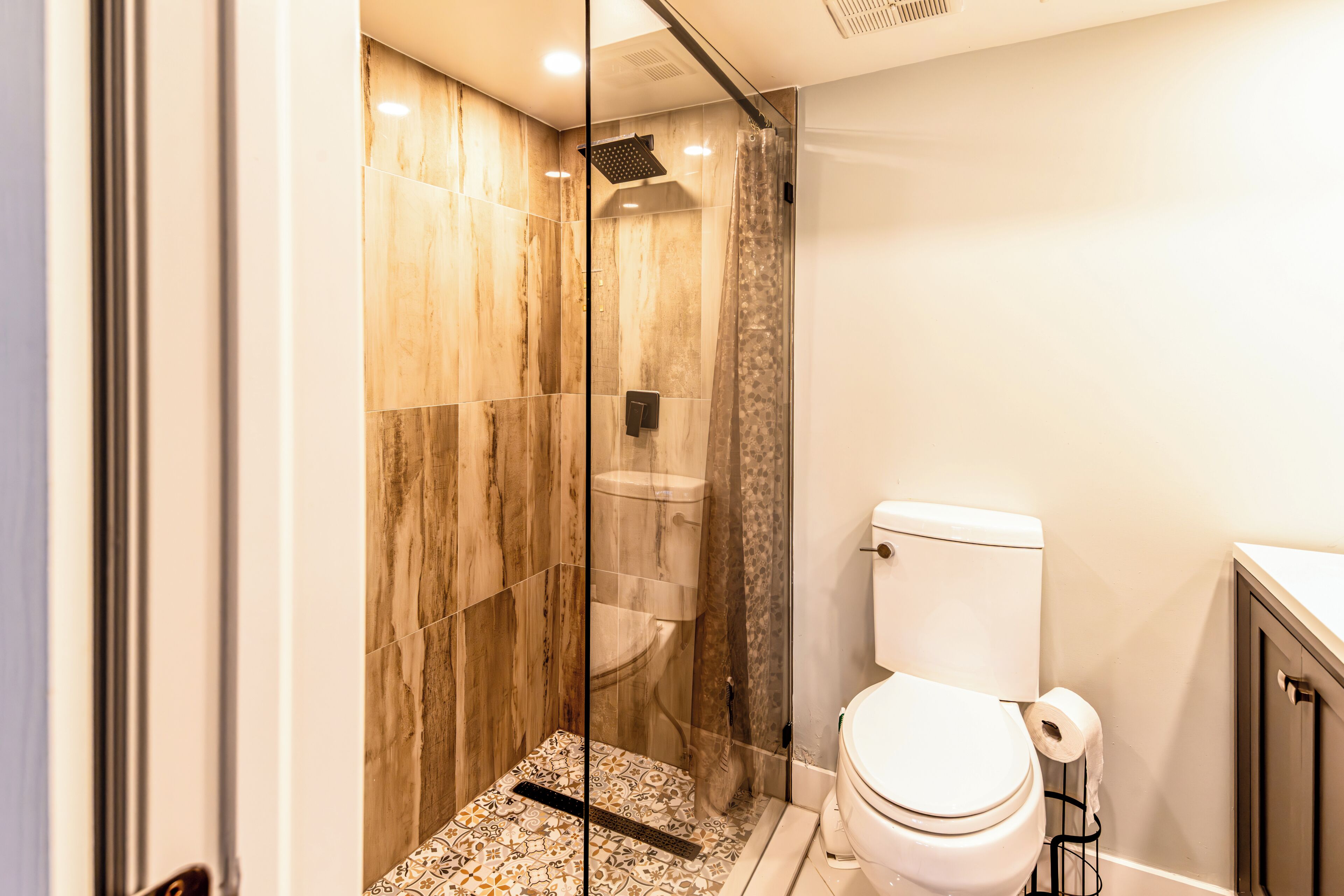 A modern bathroom with a glass-enclosed shower, a toilet, and patterned floor tiles.