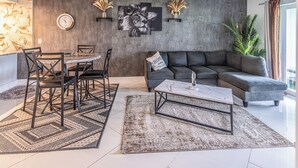 Ein modernes Wohnzimmer mit Essbereich, einem grauen Sofa, einem Couchtisch und einer Wanduhr.