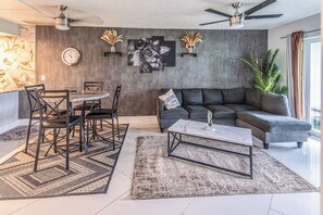 Ein modernes Wohnzimmer mit Essbereich, einem grauen Sofa, einem Couchtisch und einer Wanduhr.