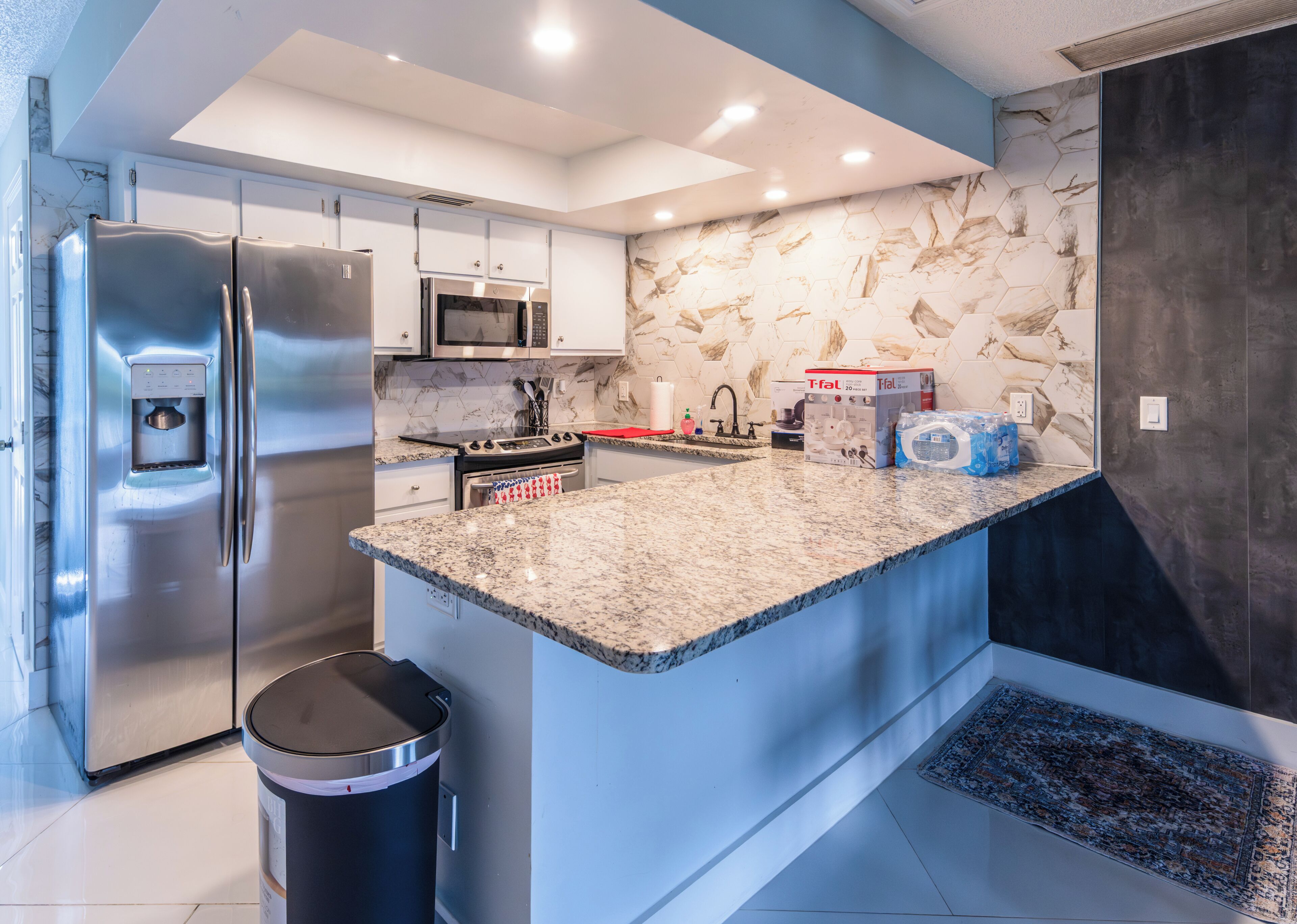 A modern kitchen with stainless steel appliances, a granite countertop, and a hexagonal tile backsplash.