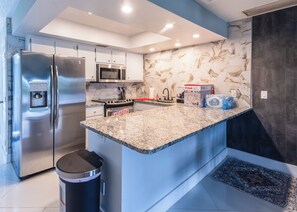 A modern kitchen with stainless steel appliances, a granite countertop, and a hexagonal tile backsplash. - Lakeside Oasis Fort Myers (Fort Myers)