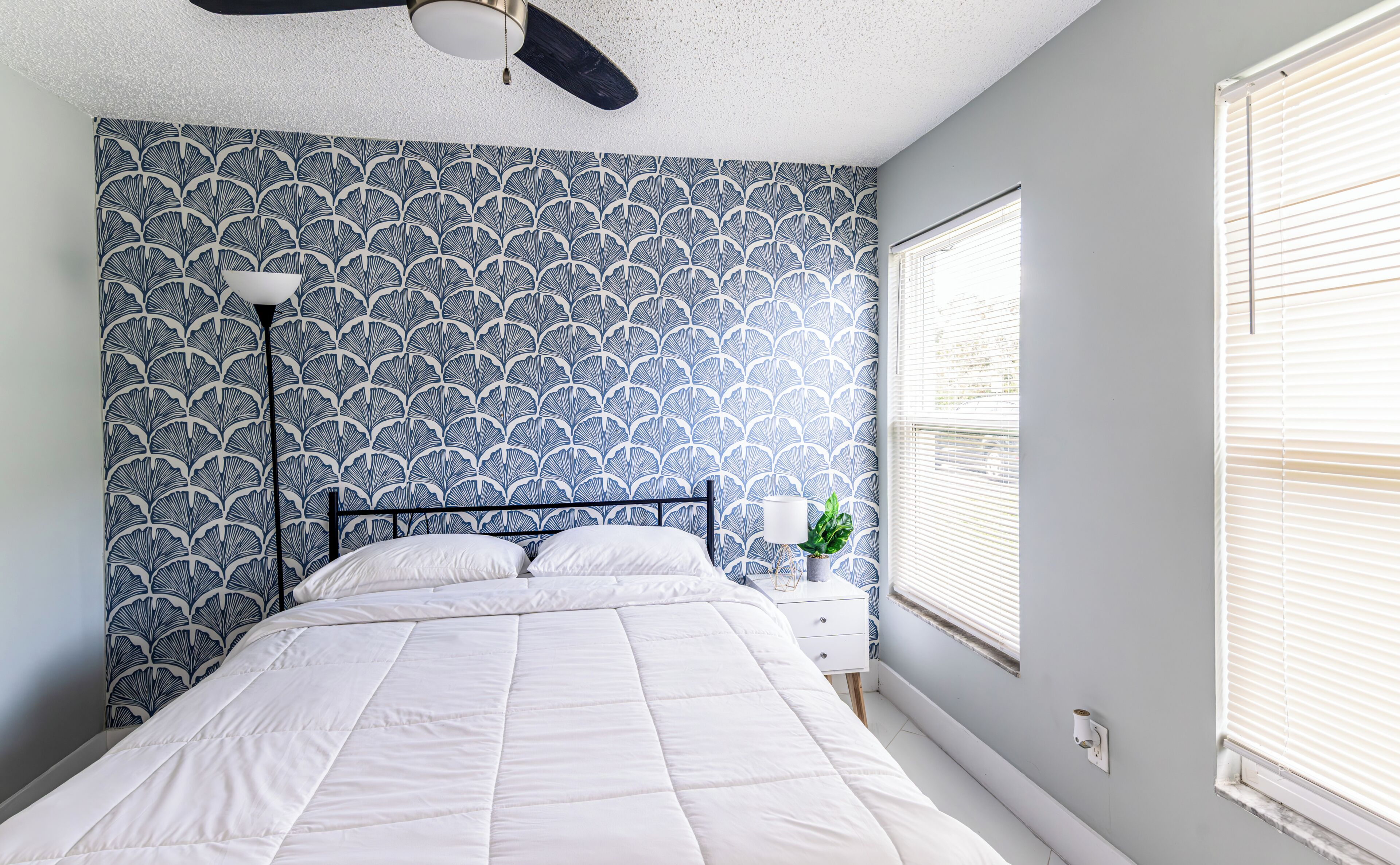 A bedroom with a bed, a nightstand, a lamp, and a window with blinds.