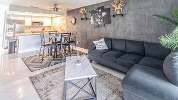 Un salon moderne avec un canapé gris, une table basse et un coin repas comprenant des chaises et une table.