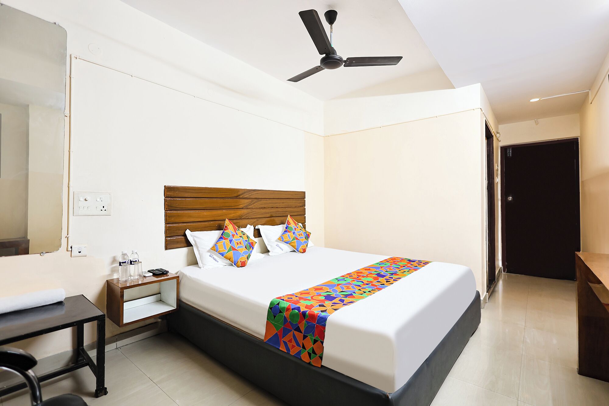 Une chambre d’hôtel avec un lit, un bureau, une chaise, un ventilateur de plafond et une porte.